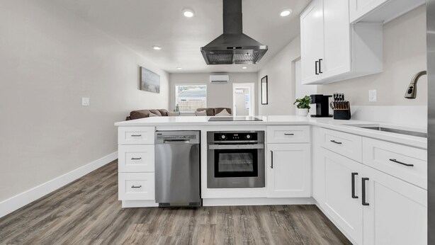 Una cocina moderna con armarios blancos, lavavajillas de acero inoxidable, horno y campana extractora negra.