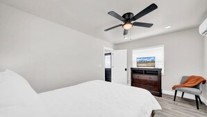 Un dormitorio con cama, cómoda, silla, ventilador de techo y ventana con persianas.