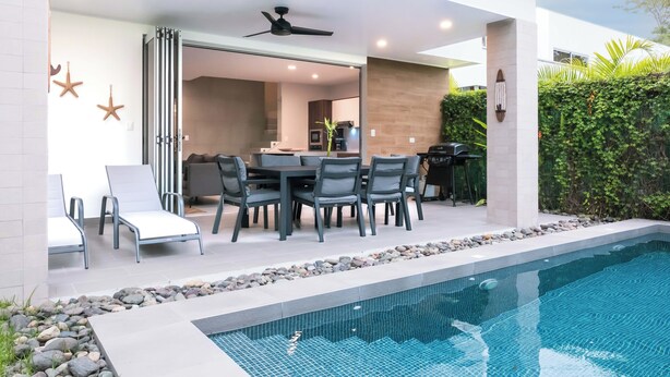 Un área de piscina exterior moderna con un comedor y un ventilador de techo.