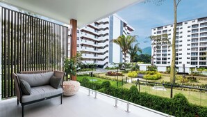 Un balcón con sofá, una gran piedra decorativa y vistas a un jardín cuidado y edificios modernos.