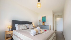 A neatly made bed with a striped bedspread, a bedside lamp, and a vase with flowers on a bedside table.