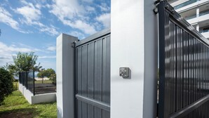 A gated entrance with a keypad lock, a white wall, and a metal gate.