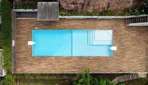 Vista aérea de una piscina rectangular con dos sillas de descanso, rodeada por un muelle de madera y un muro de piedra.