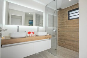 A modern bathroom with a wooden vanity, two sinks, a glass shower enclosure, and a large mirror.
