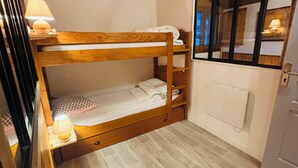 Un lit superposé avec une tête de lit en bois, une lampe de chevet et une fenêtre avec des stores.