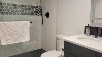 A bathroom with a white toilet, a shower with a glass door, and a sink with a black faucet.