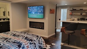 Ein modernes Hotelzimmer mit einem großen Bett, einem flachbildfernseher über einem Kamin, einer Küchenzeile und einer Bar.