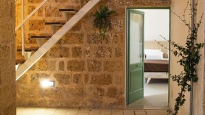 Un escalier dans un bâtiment aux murs de pierre, avec une porte verte donnant sur une pièce où se trouve un lit.