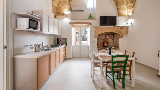 Une cuisine aux murs en pierre, un coin repas avec une table et des chaises, et un téléviseur fixé au-dessus de la cheminée.