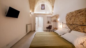 Une chambre à coucher avec un lit, un téléviseur fixé au mur, une chaise et une petite table.