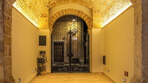 Un corredor de piedra en arco con una verja metálica al final, que conduce a una habitación con suelo de baldosas.