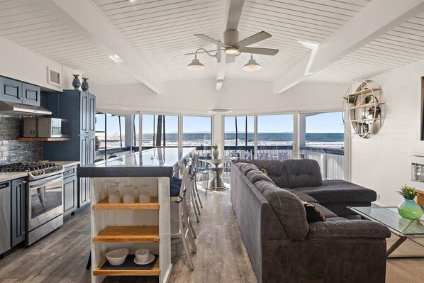 Eine moderne Küche mit Meerblick, ein großes graues Sofa und ein Essbereich mit hoher Decke und großen Fenstern.