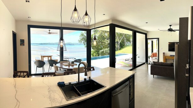 A modern kitchen with a large island, a dining area with chairs, and a view of the ocean. - Escape to your oceanfront retreat: Sea La Vie! (Playa Hermosa Boca Chica)