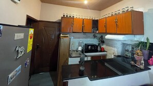 Une cuisine de taille réduite, dotée de meubles de rangement en bois, d’un réfrigérateur, d’un four à micro-ondes et d’un évier.