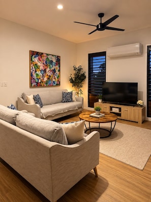 A modern living room with a sofa, coffee table, and a flat-screen TV. - Kookaburra - A Home in the Trees (Cannon Valley)