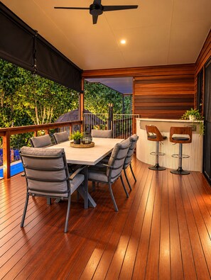An outdoor patio with a wooden table and chairs, a ceiling fan, and a view of greenery. - Kookaburra - A Home in the Trees (Cannon Valley)