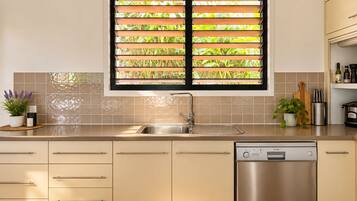 Una cocina moderna con lavavajillas de acero inoxidable, un lavaplatos y una ventana con persianas.