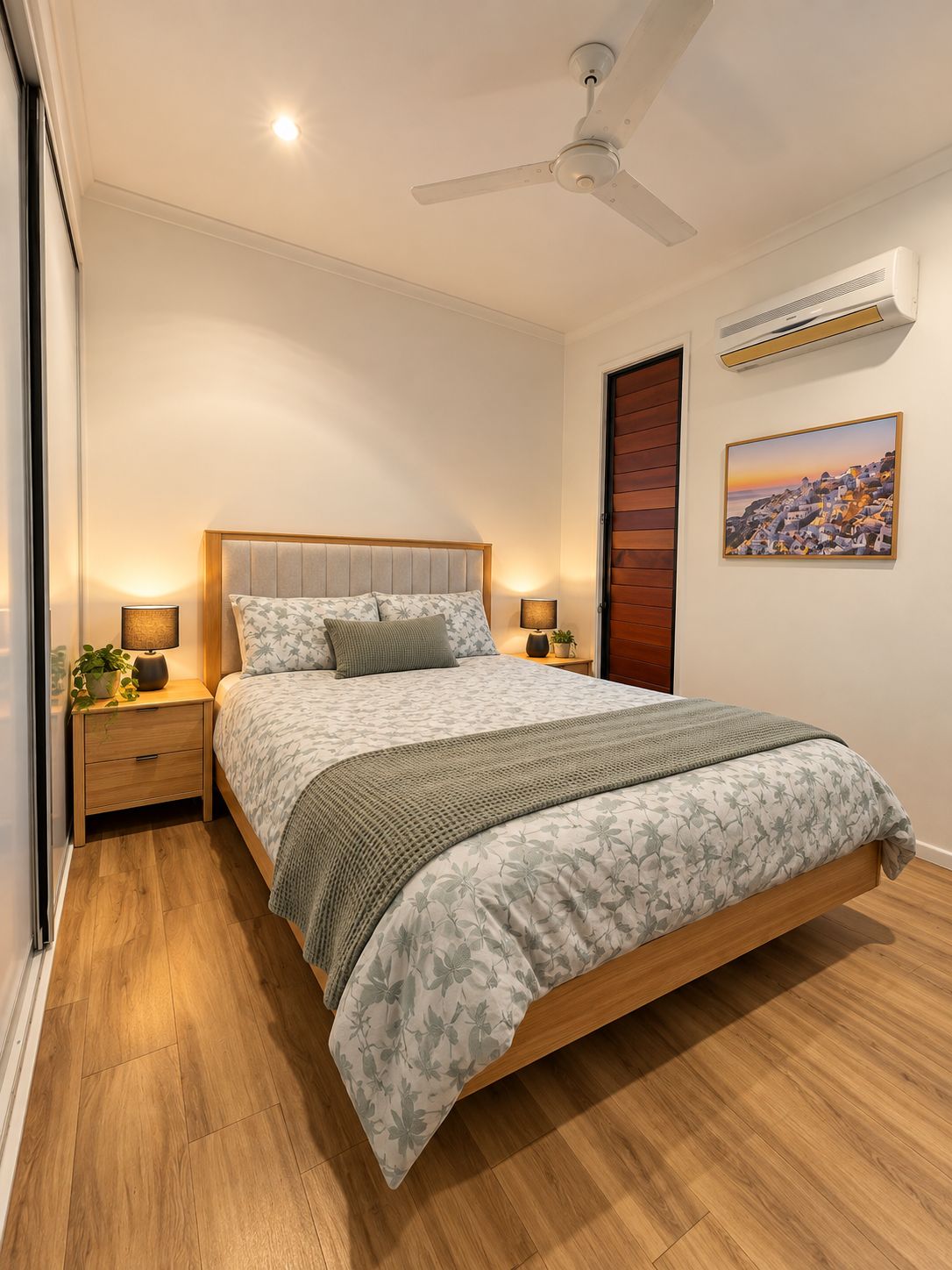A bedroom with a bed, nightstands, a ceiling fan, an air conditioning unit, and a painting on the wall.
