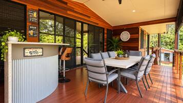 A modern outdoor dining area with a wooden deck, a bar counter, and a ceiling fan.