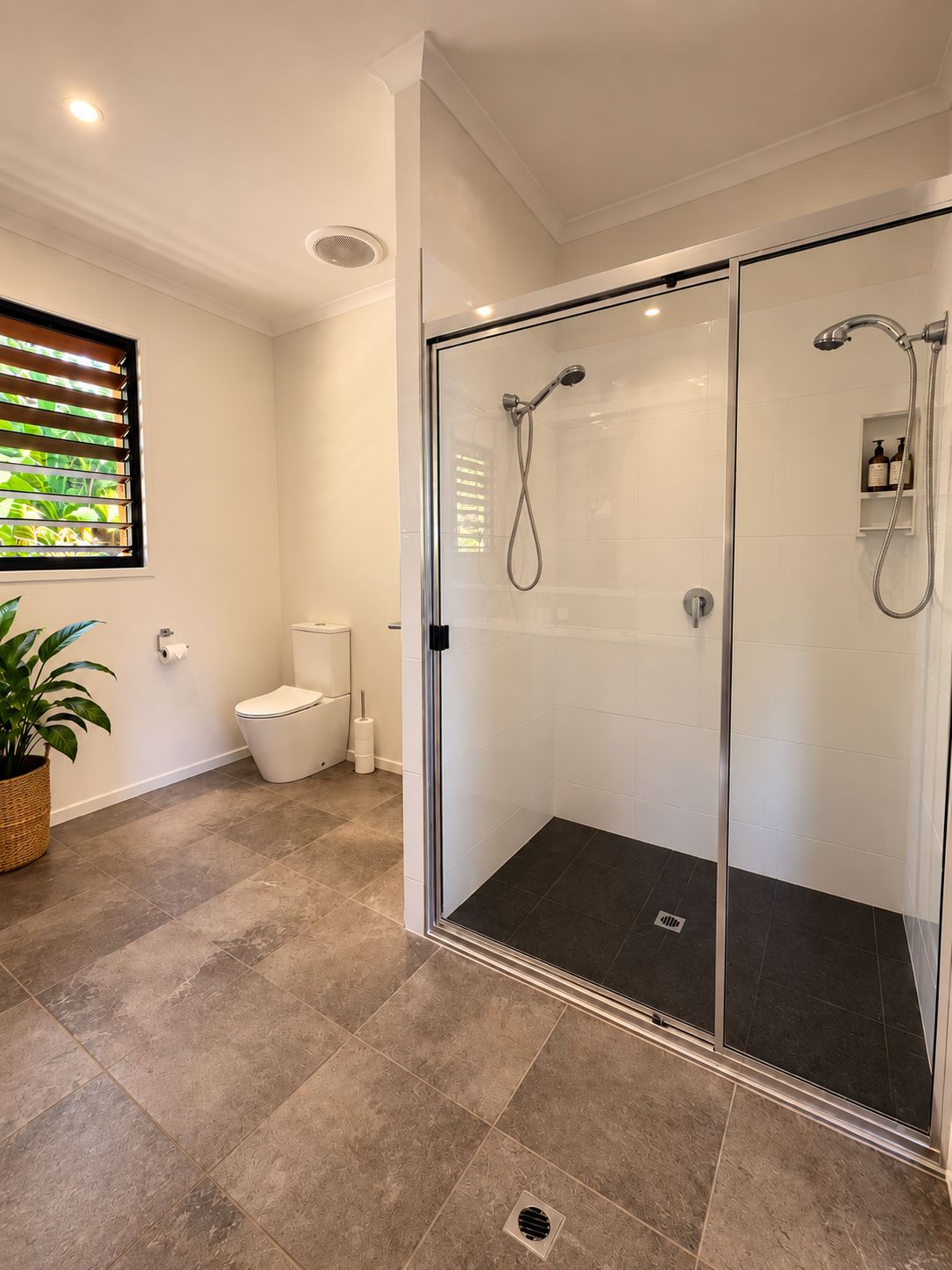 Un baño moderno con ducha envuelta en vidrio, inodoro y una planta en maceta.