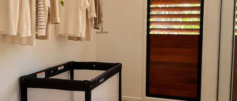 Una habitación con cuna, perchero, cesta y cesto tejido, además de una ventana con persianas.