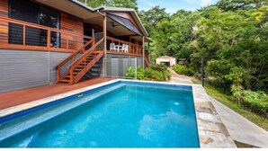 Ein modernes Haus mit Schwimmbad, einer Holzterrasse und einem überdachten Außenbereich mit Treppe zu einem Balkon.