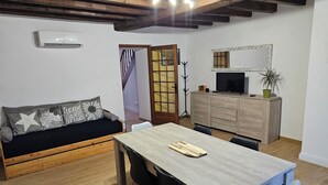 Un salon chaleureux avec un canapé en bois, une table à manger et un téléviseur posé sur un meuble en bois.