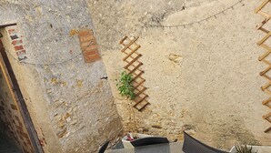 Un espace extérieur aménagé avec un mur en pierre, une échelle en bois et un pot de fleurs.