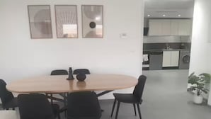 Een moderne eethoek met een ronde tafel en zwarte stoelen, een keuken op de achtergrond en een potplant aan de rechterkant.