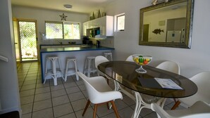 A modern kitchen with white bar stools, a glass dining table, and a large mirror on the wall. - Villa 51 - Tangalooma - Moreton Island (moreton island)