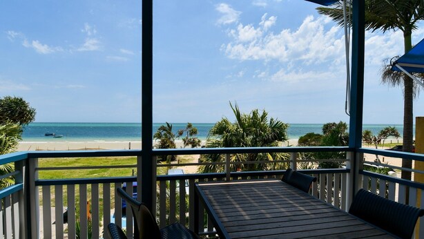 A wooden deck with a bench and a table, overlooking a beach with palm trees and the ocean. - Villa 51 - Tangalooma - Moreton Island (moreton island)