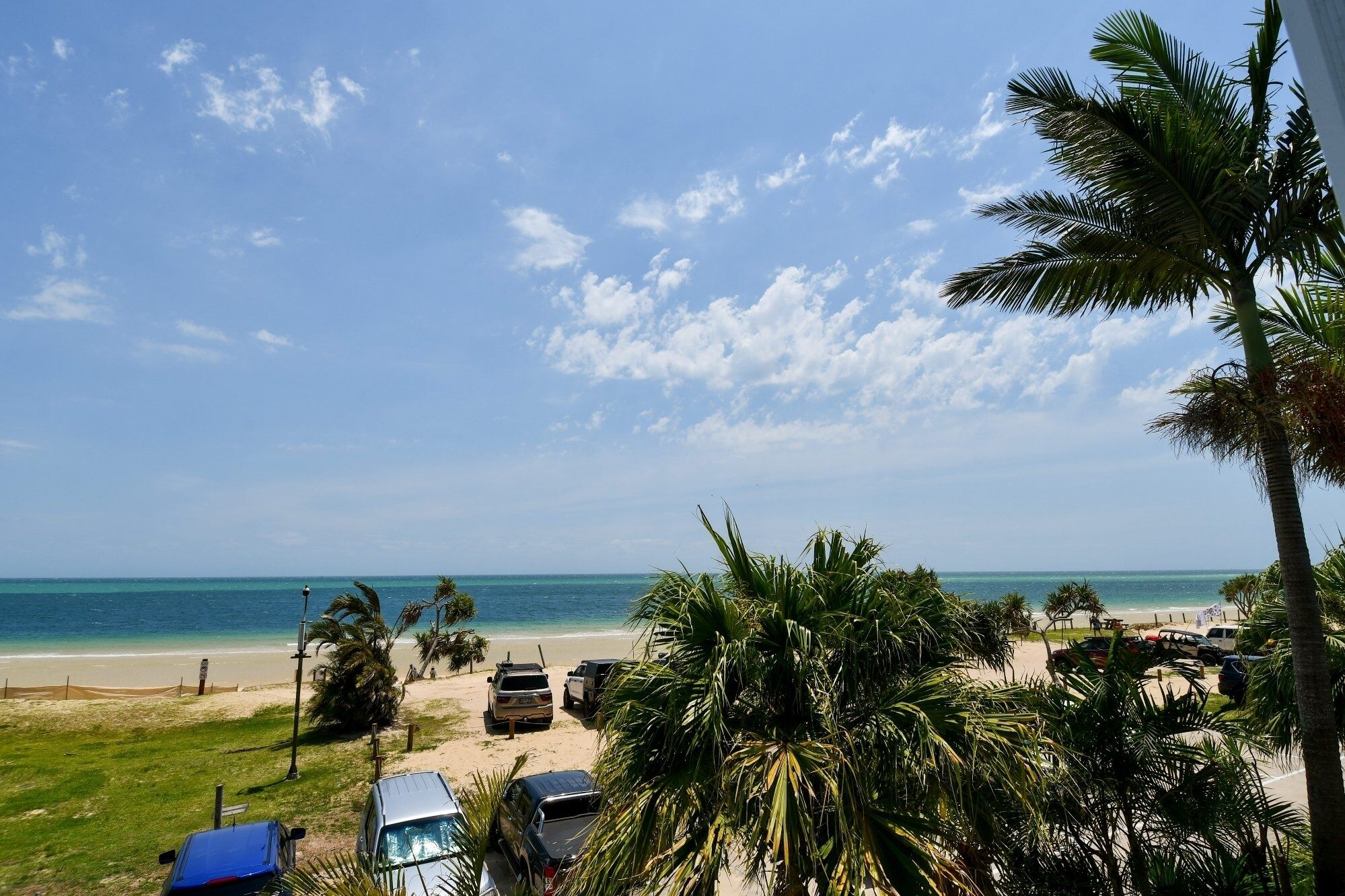 Une vue sur la plage, avec des voitures garées, des palmiers et un ciel dégagé.