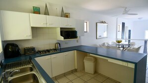 A modern kitchen with white cabinets, a blue countertop, a gas stove, a microwave, and a sink. There is a small trash bin and a ceiling fan. - Villa 51 - Tangalooma - Moreton Island (moreton island)