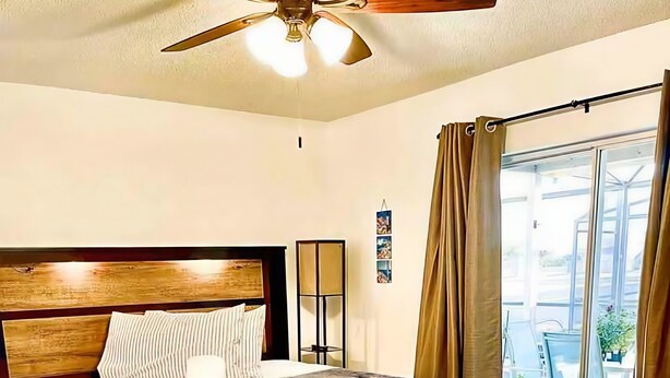 Ein Schlafzimmer mit einem Bett, einem Deckenventilator, einer Stehlampe und Blick ins Freie.