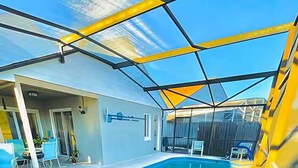 Ein Schwimmbecken mit Glasüberdachung, eine Terrasse mit Stühlen und Tisch sowie ein überdachter Außenbereich.