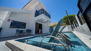 A modern building with a pool area, including lounge chairs and a dining area.