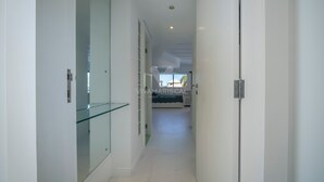 A modern hallway with glass doors, a view into a room with a bed, and a ceiling light.