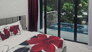A modern bedroom with a large bed, a ceiling fan, an air conditioning unit, and a view of a swimming pool and greenery outside.