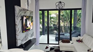 A modern living room with a white sofa, a marble fireplace, and a large sliding glass door leading to a balcony with a view of greenery.