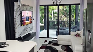 A modern living room with a large TV, a white sofa, and a kitchen area.