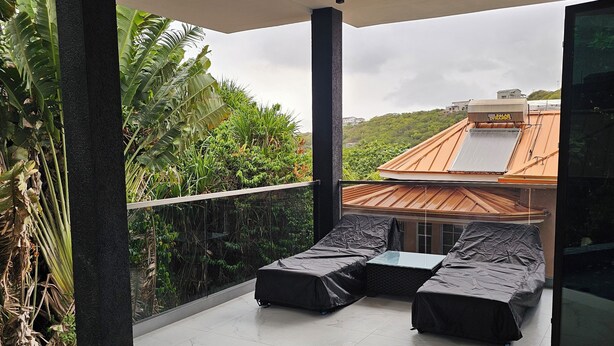 A modern outdoor pool area with a tiled floor, a hot tub, and two covered lounge chairs.