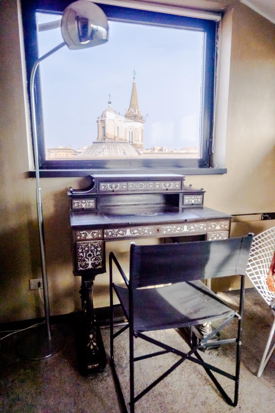 A desk with a chair, a lamp, and a window with a view of a building.