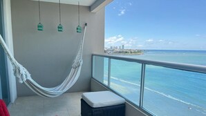 A balcony with a hammock, a red chair, and a wicker ottoman. - Oceánica Luxury Apartment (Salinas)