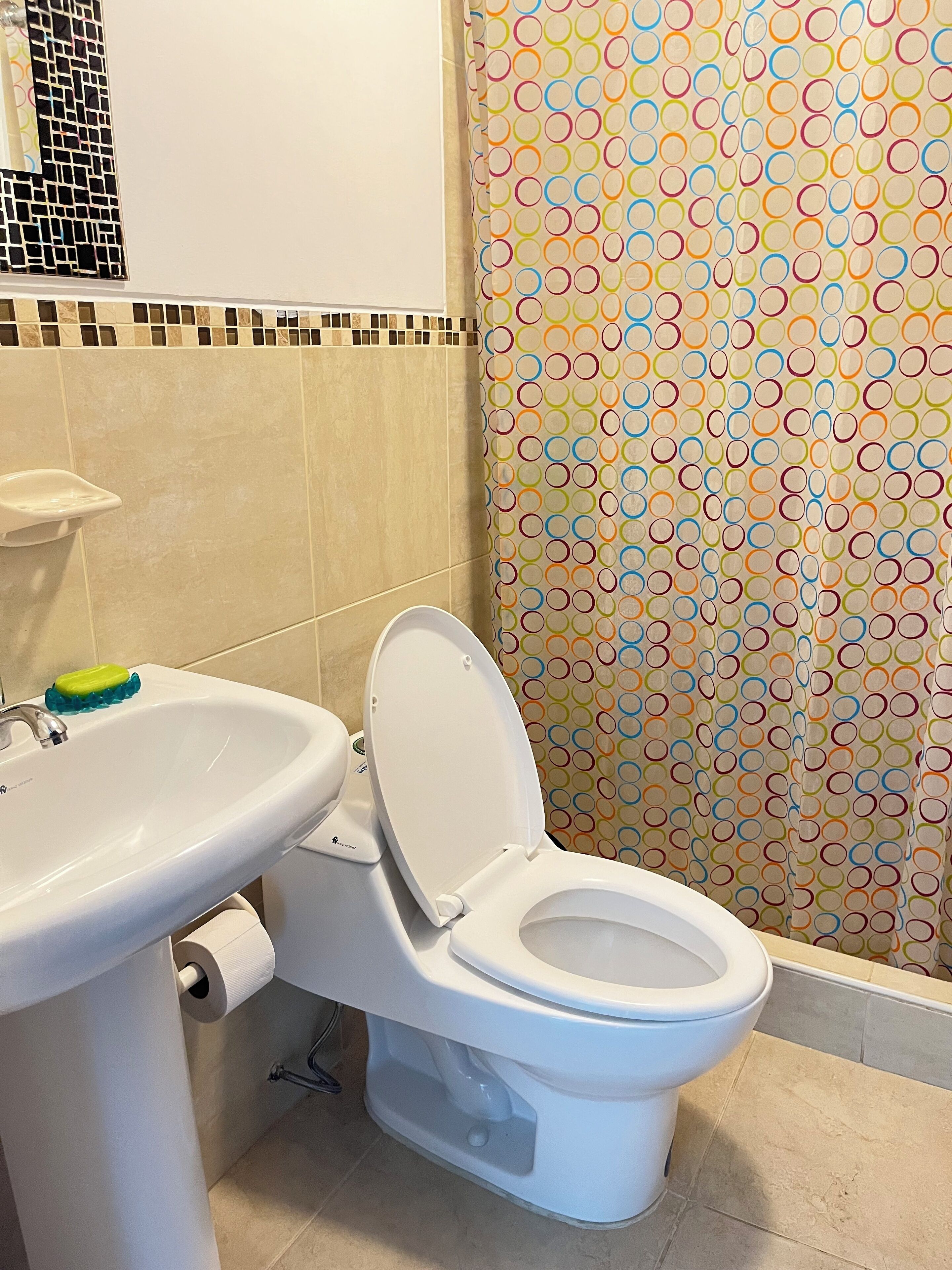 Een badkamer met toilet, wastafel en een douchegordijn met een kleurrijk rond patroon.