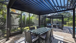 Ein überdachter Patio mit Glasveranda, Gartenmöbeln und Blick auf einen Swimmingpool.