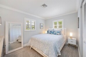 Une chambre à coucher avec un grand lit, une table de chevet, un miroir et une fenêtre avec des volets.