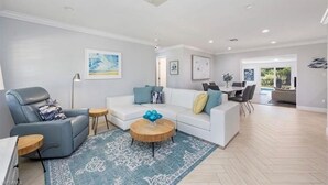 Ein geräumiges Wohnzimmer mit einem weißen Sofa, einem blauen Sessel und einem runden Couchtisch.