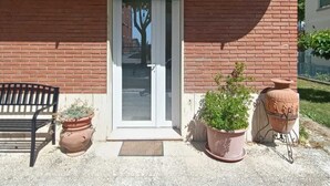 A brick building with a white door and a small porch. There are two potted plants and a bench outside. - Elegance and relaxation in an exclusive ground floor apartment flooded with light. (Carpegna)