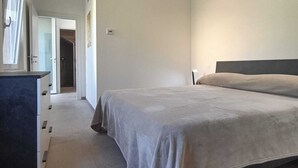 A bedroom with a bed, a dresser, a door leading to another room, and a chandelier. - Elegance and relaxation in an exclusive ground floor apartment flooded with light. (Carpegna)