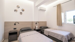 Una habitación de hotel moderna con dos camas, una mesita de noche, aire acondicionado de pared y una ventana con cortinas.